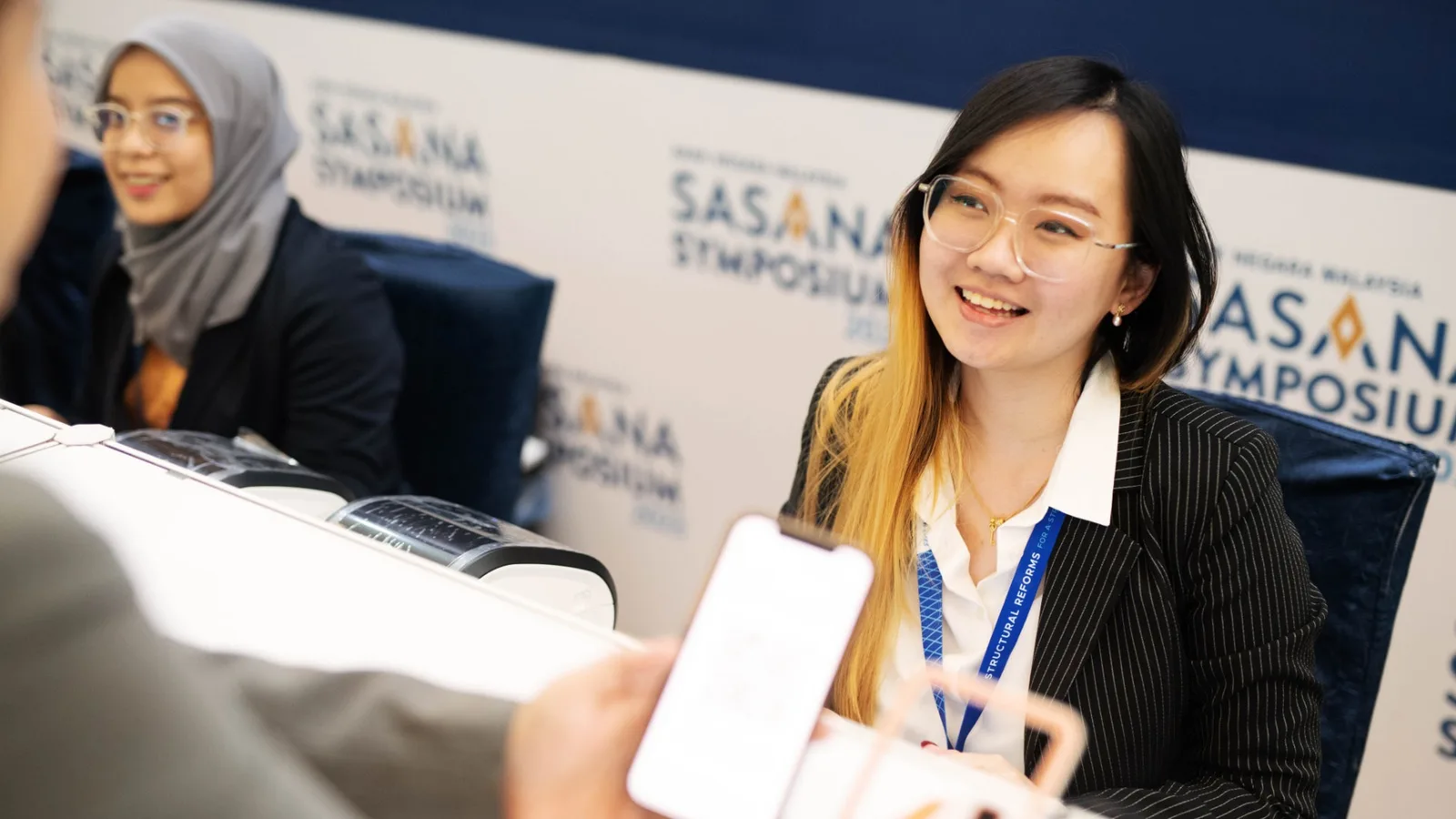 Attendees checking in at the Sasana Symposium registration desk with a QR code